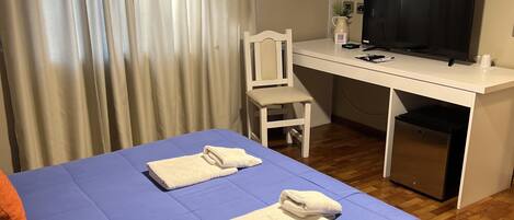 A room with a bed, a desk, a chair, a television, and an air conditioning unit.