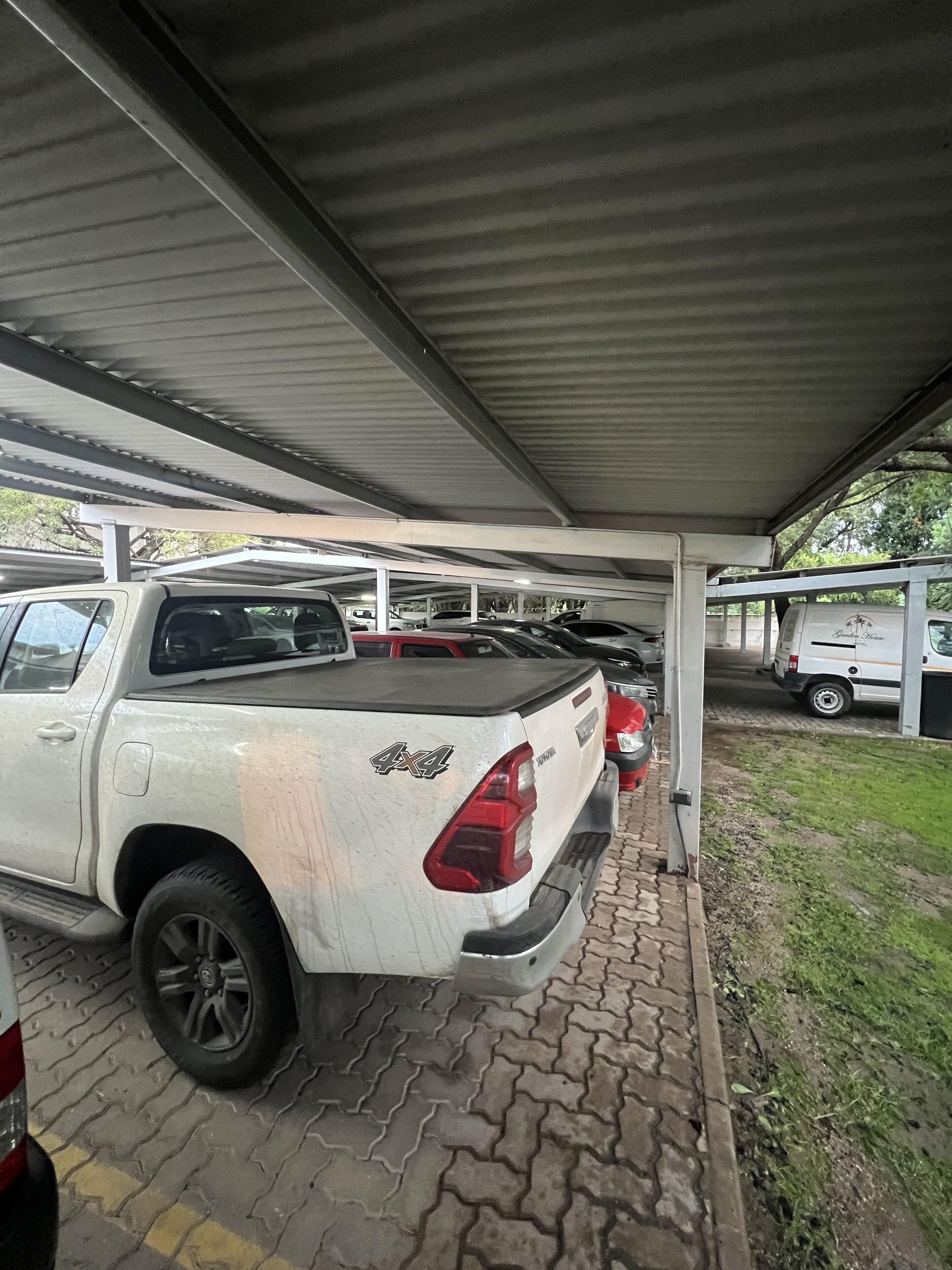 Un área de estacionamiento techada con una camioneta blanca estacionada bajo un techo metálico.