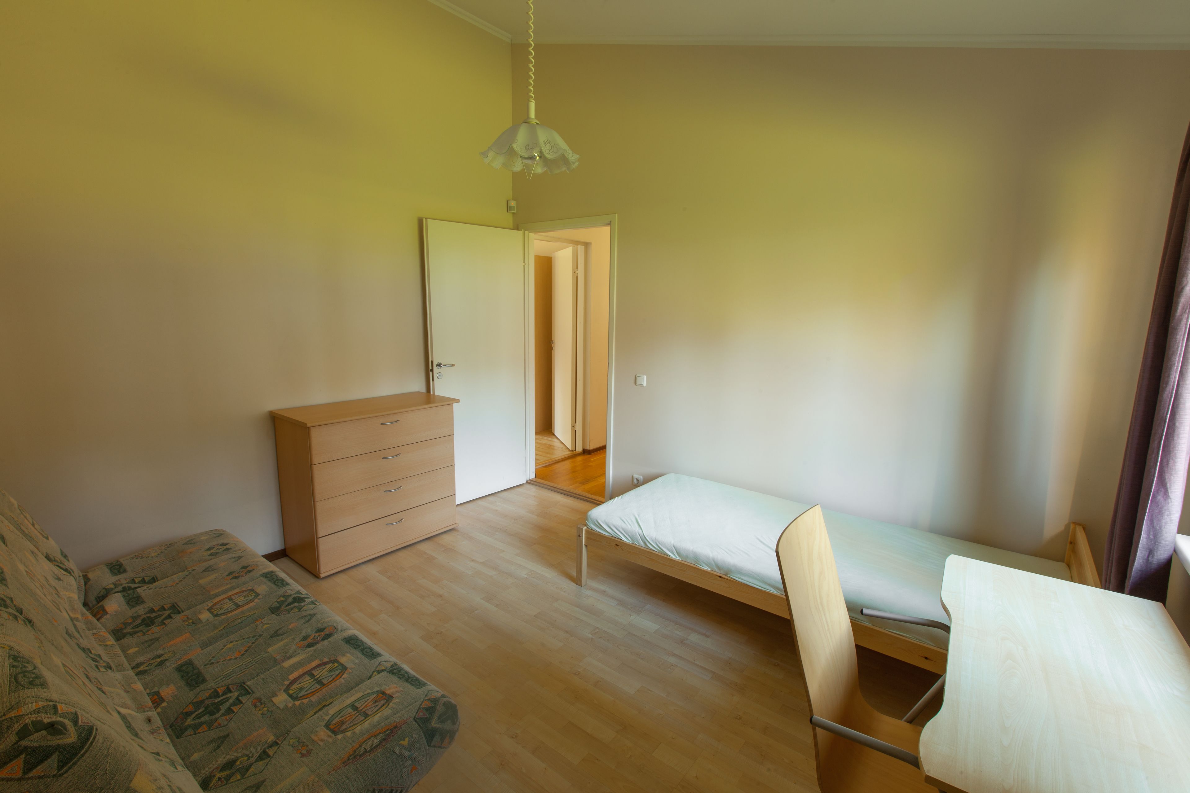 Een slaapkamer met een bed, een houten dressoir, een stoel en een bijzettafeltje.
