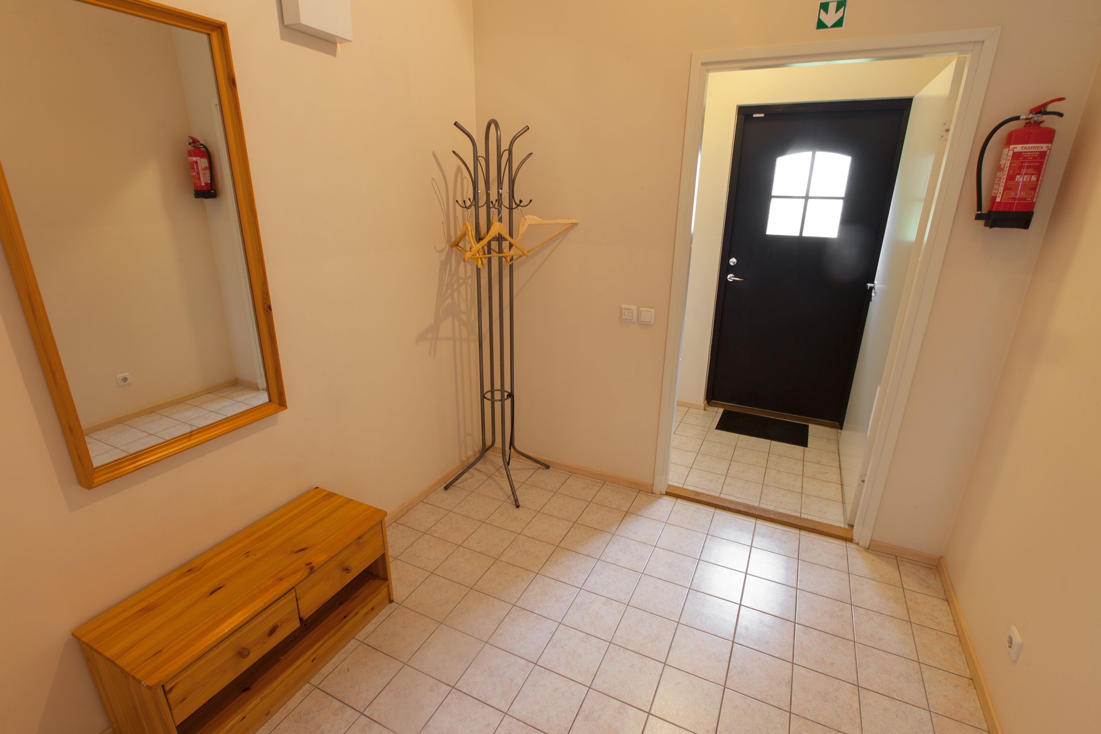 A hallway with a wooden bench, a coat rack, a fire extinguisher, and a door with a window.