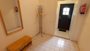 A hallway with a wooden bench, a coat rack, a fire extinguisher, and a door with a window.