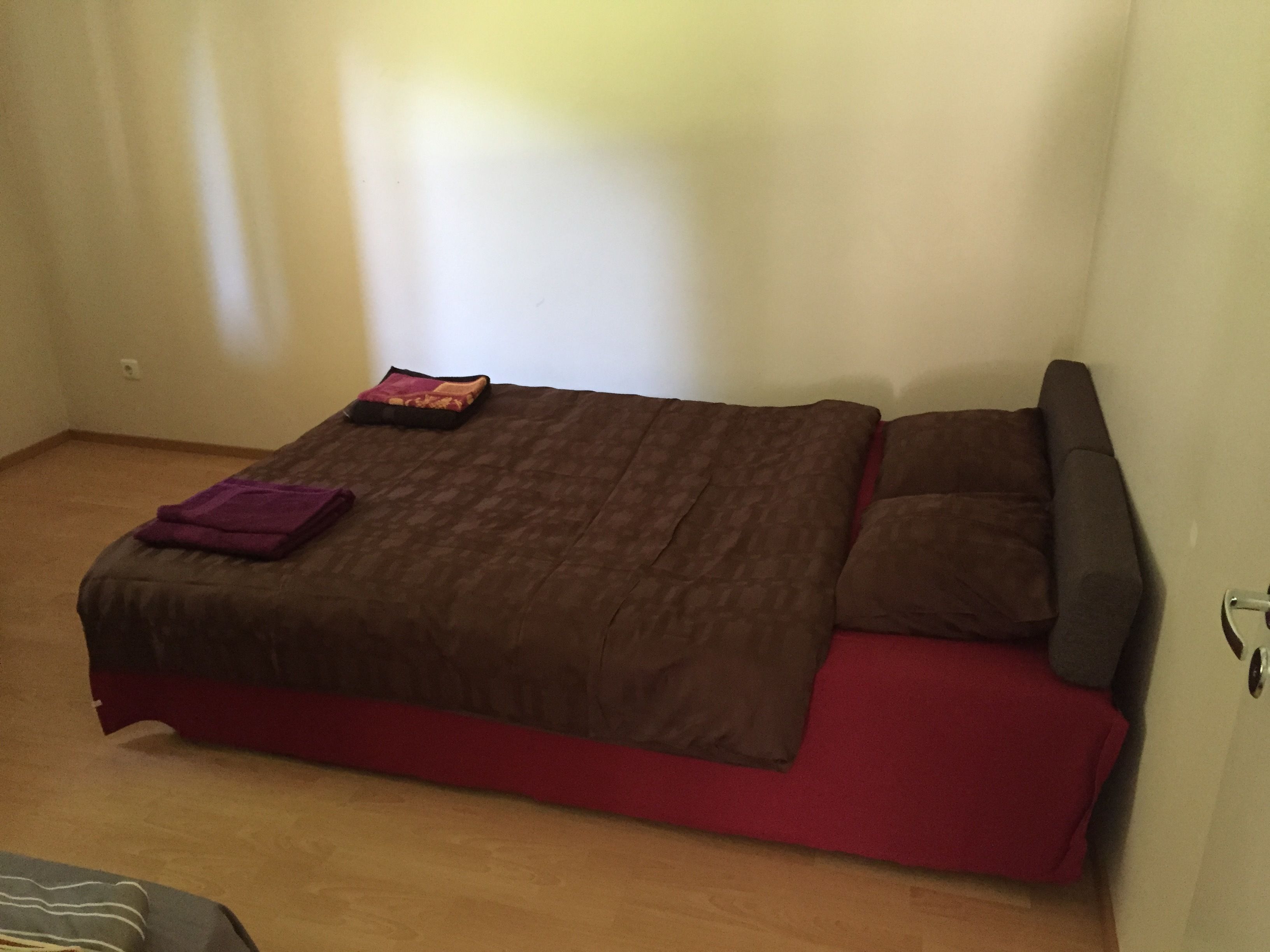 Uma cama de solteiro com um cobre-leito marrom e vermelho, um cobertor roxo e duas almofadas.