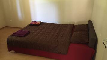 Uma cama de solteiro com um cobre-leito marrom e vermelho, um cobertor roxo e duas almofadas.