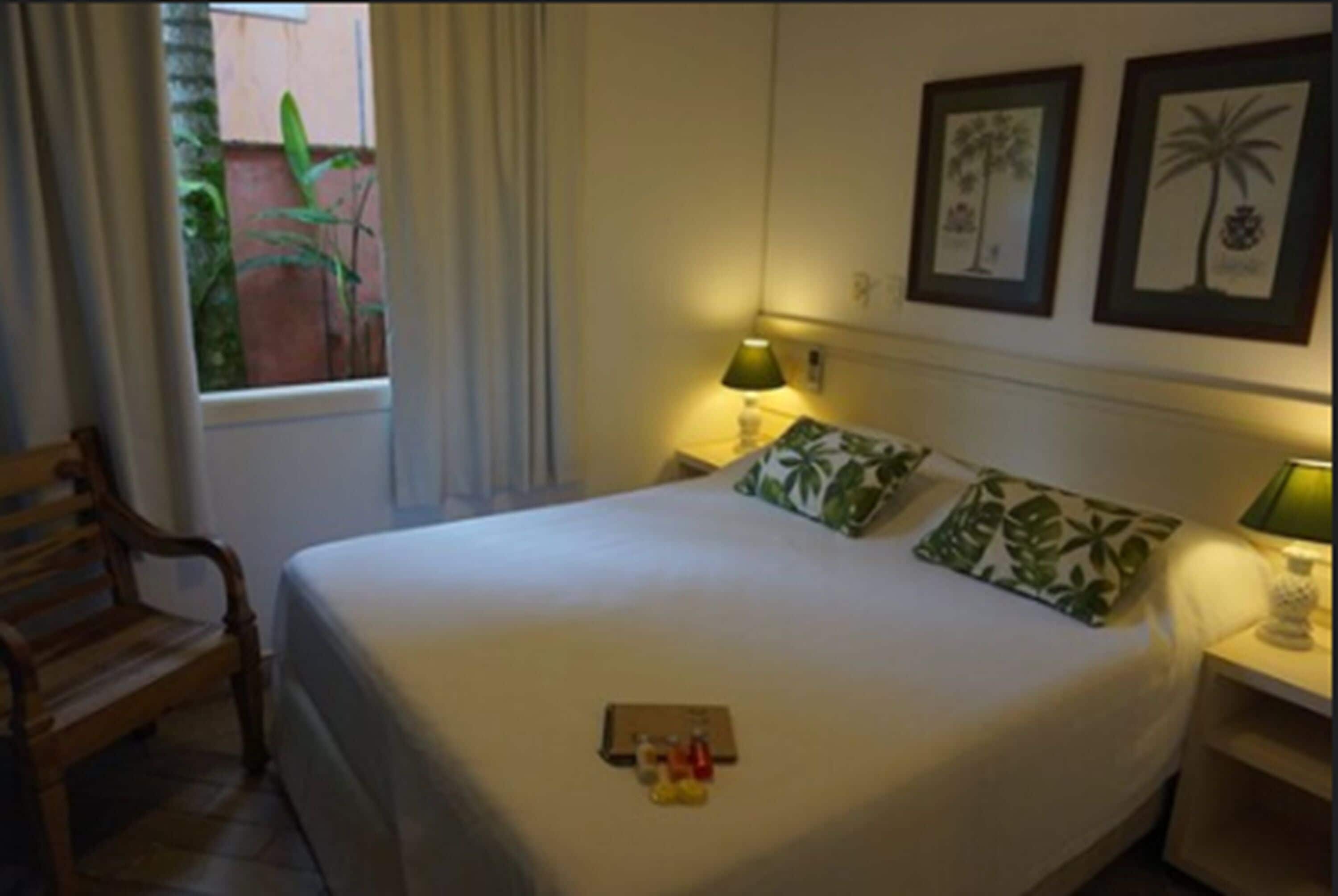 A neatly made bed with a pillow, a bedside table with a lamp, and a window with curtains.