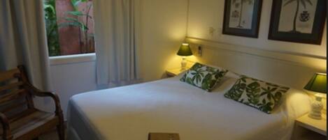 A neatly made bed with a pillow, a bedside table with a lamp, and a window with curtains.