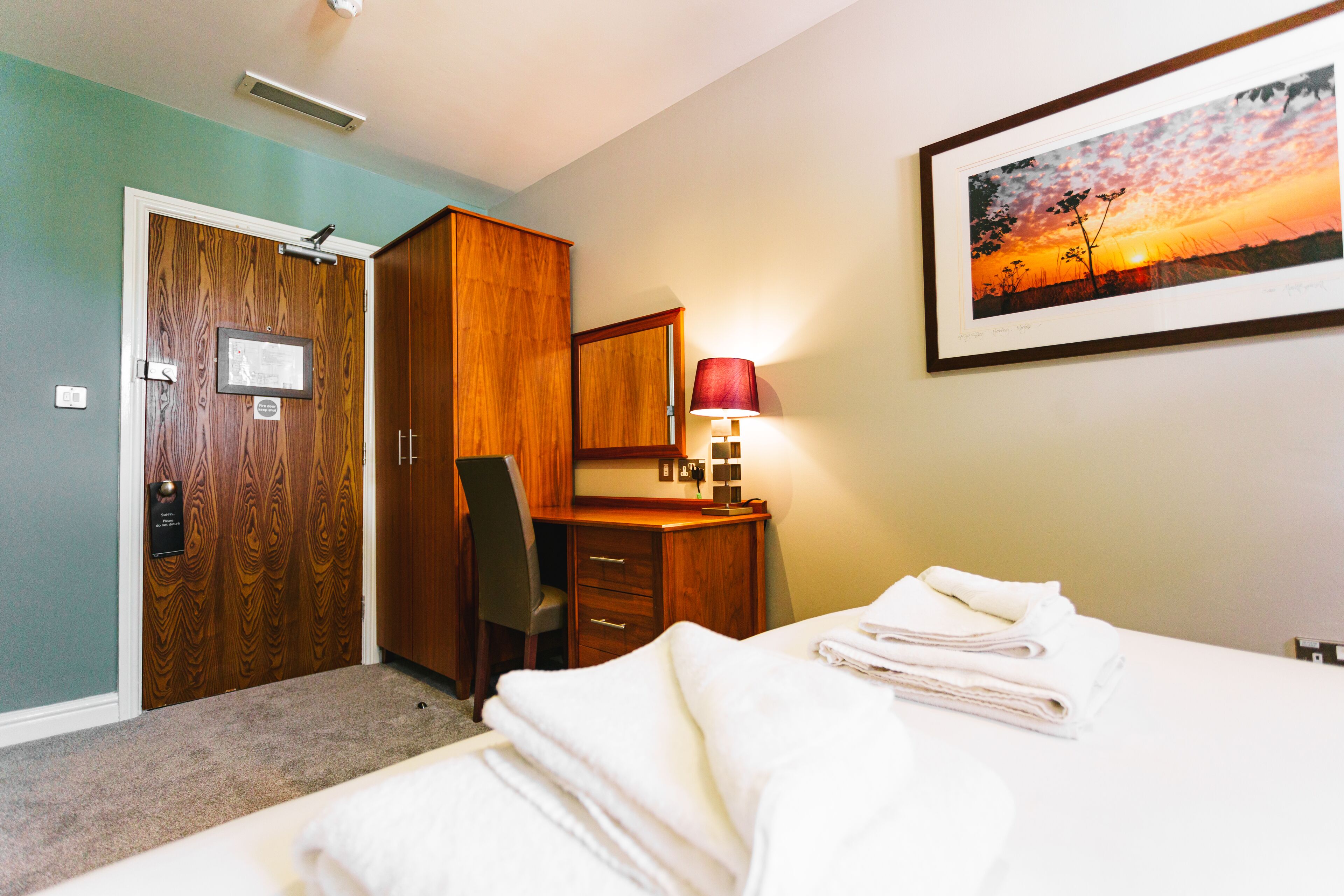 Ein Hotelzimmer mit Bett, Schreibtisch, Stuhl, Kleiderschrank und einem gerahmten Bild an der Wand.