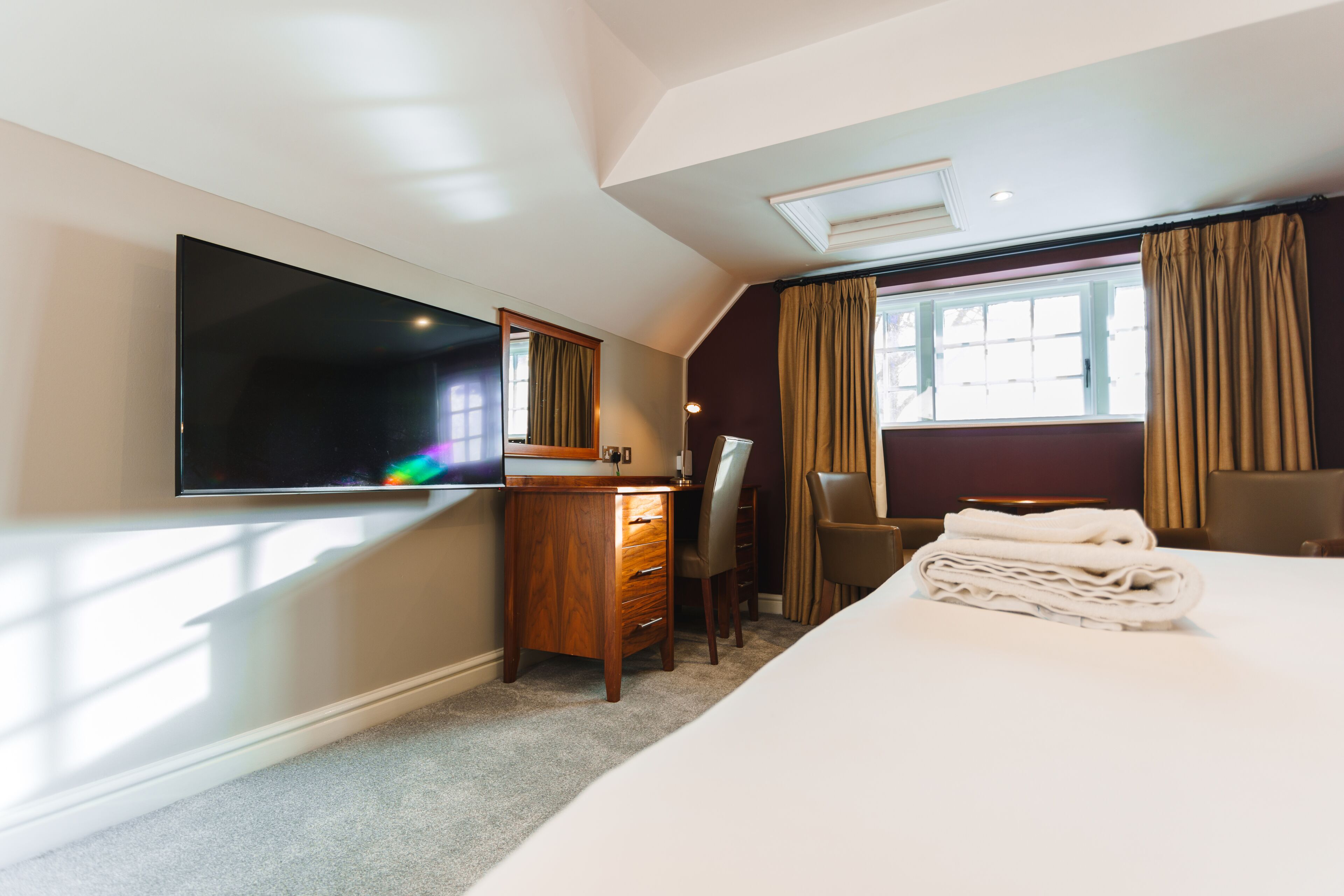 Een hotelkamer met een bed, een bureau met stoel, een televisie en een raam met gordijnen.