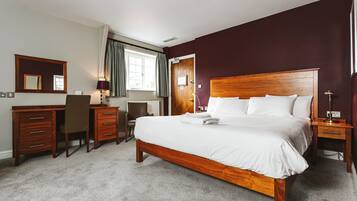 A hotel room with a wooden bed, a desk with drawers, a chair, a mirror, and a window with curtains.