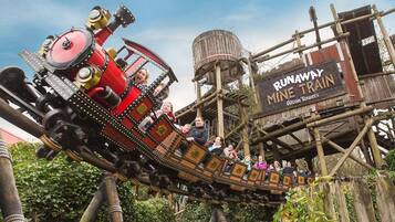 A wooden roller coaster with passengers, surrounded by a rustic wooden structure and greenery.