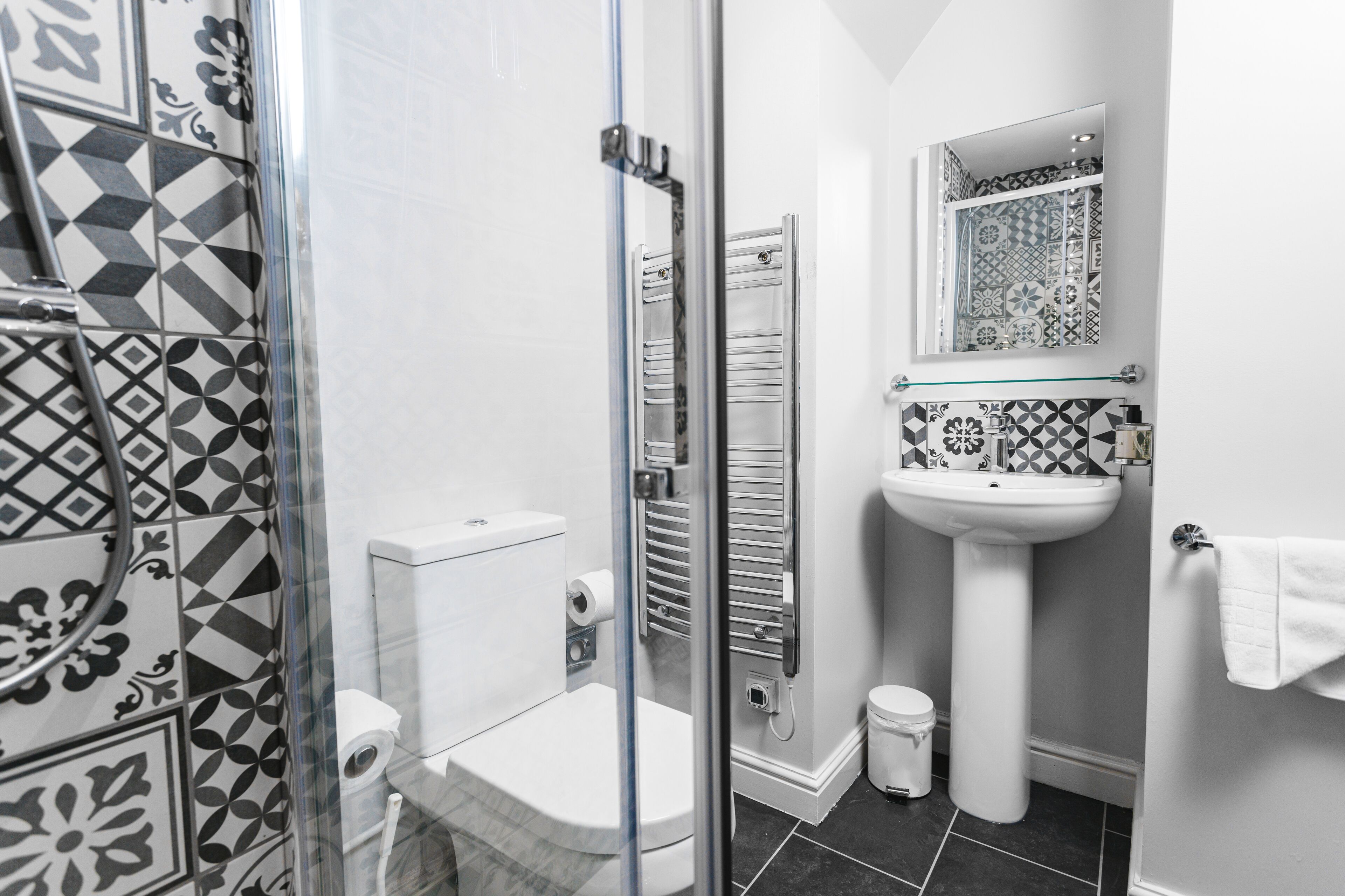 A bathroom with a glass shower enclosure, a toilet, a sink, and a mirror.