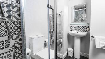 A bathroom with a glass shower enclosure, a toilet, a sink, and a mirror.