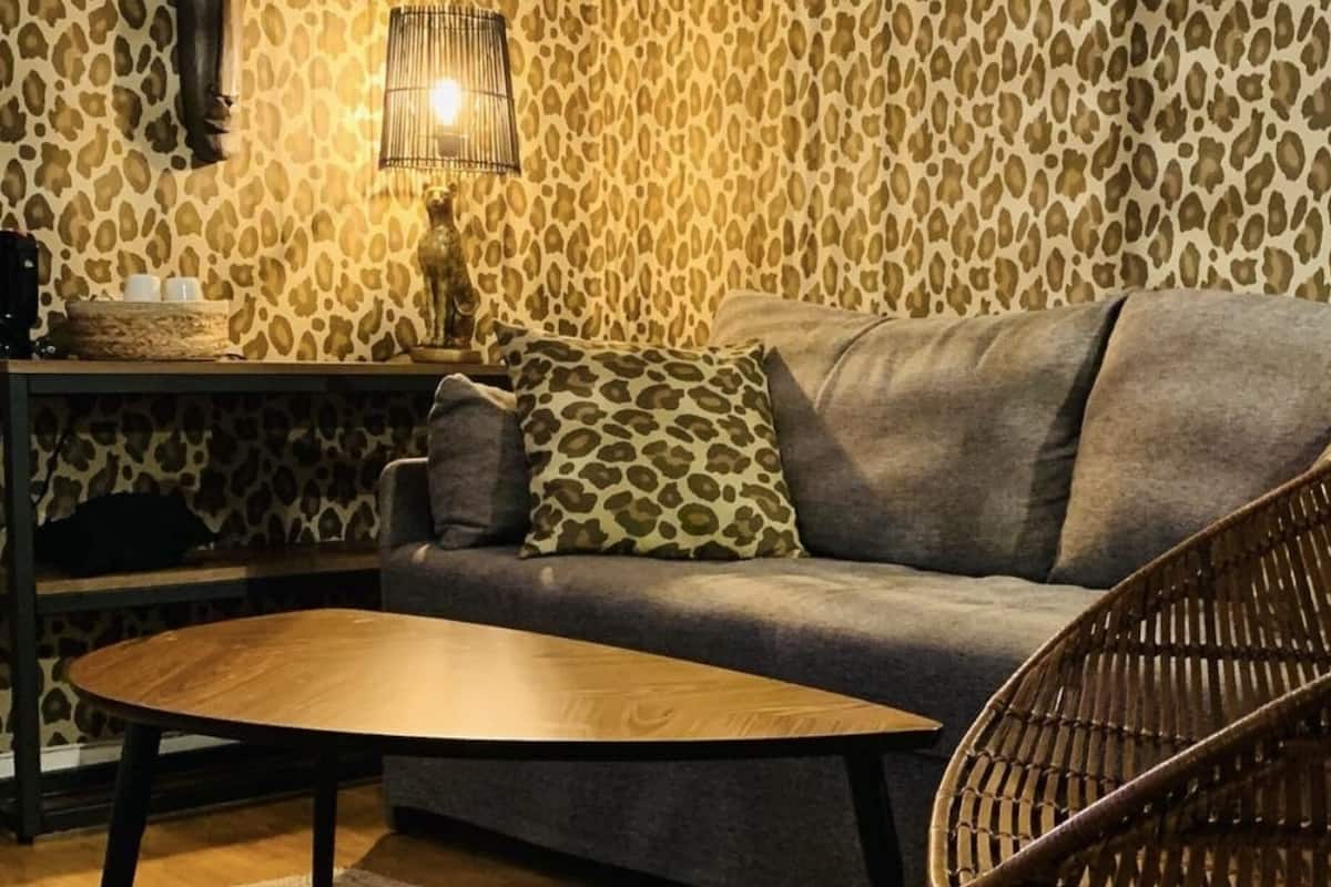 Un salon chaleureux avec un canapé gris, une table basse en bois, un fauteuil en osier et un mur décoré d’un motif léopard.