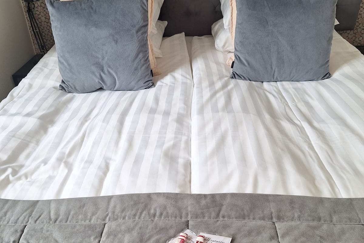 Un lit avec une literie à rayures, deux oreillers et une tête de lit rembourrée de couleur grise.