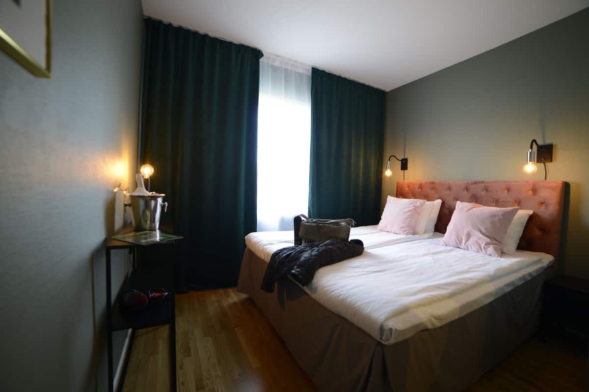 Une chambre d’hôtel avec un lit, une table de chevet, une lampe et une fenêtre avec des rideaux.