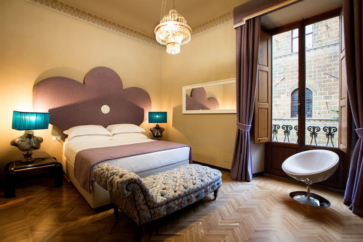 A bedroom with a bed, bedside lamps, a bench, a chair, and a chandelier.