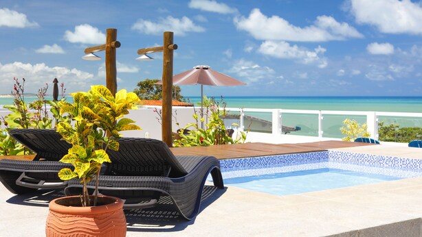 A poolside area with lounge chairs, a potted plant, and a view of the ocean. - Pipa Centro Residence (Tibau do Sul)