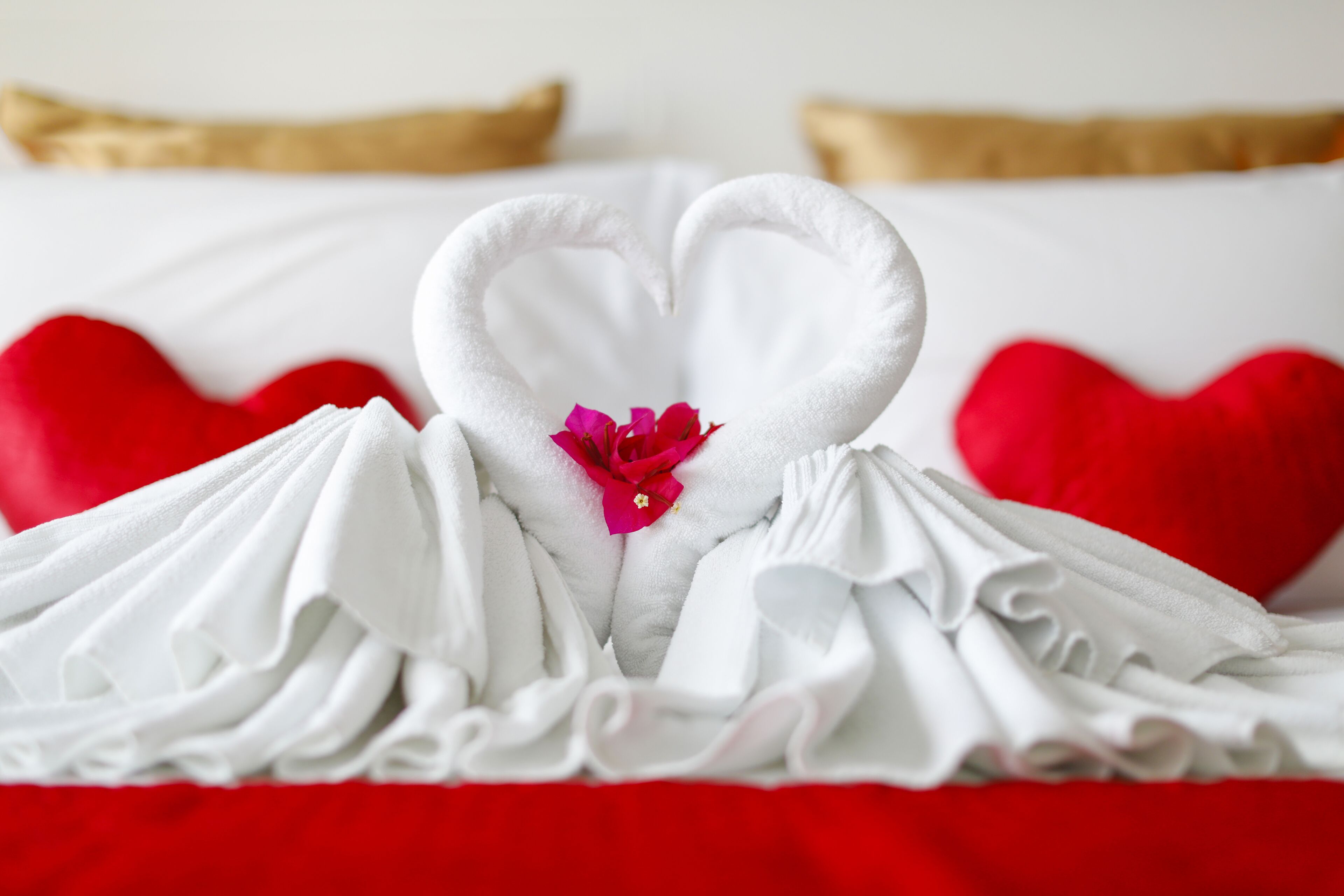 Una cama con una toalla dispuesta en forma de corazón y almohadas rojas.