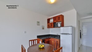 A compact kitchen with wooden cabinets, a white refrigerator, and a dining table with chairs. - Pipa Centro Residence (Tibau do Sul)