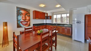A modern kitchen with wooden cabinets, a dining table, and a refrigerator. - Pipa Centro Residence (Tibau do Sul)