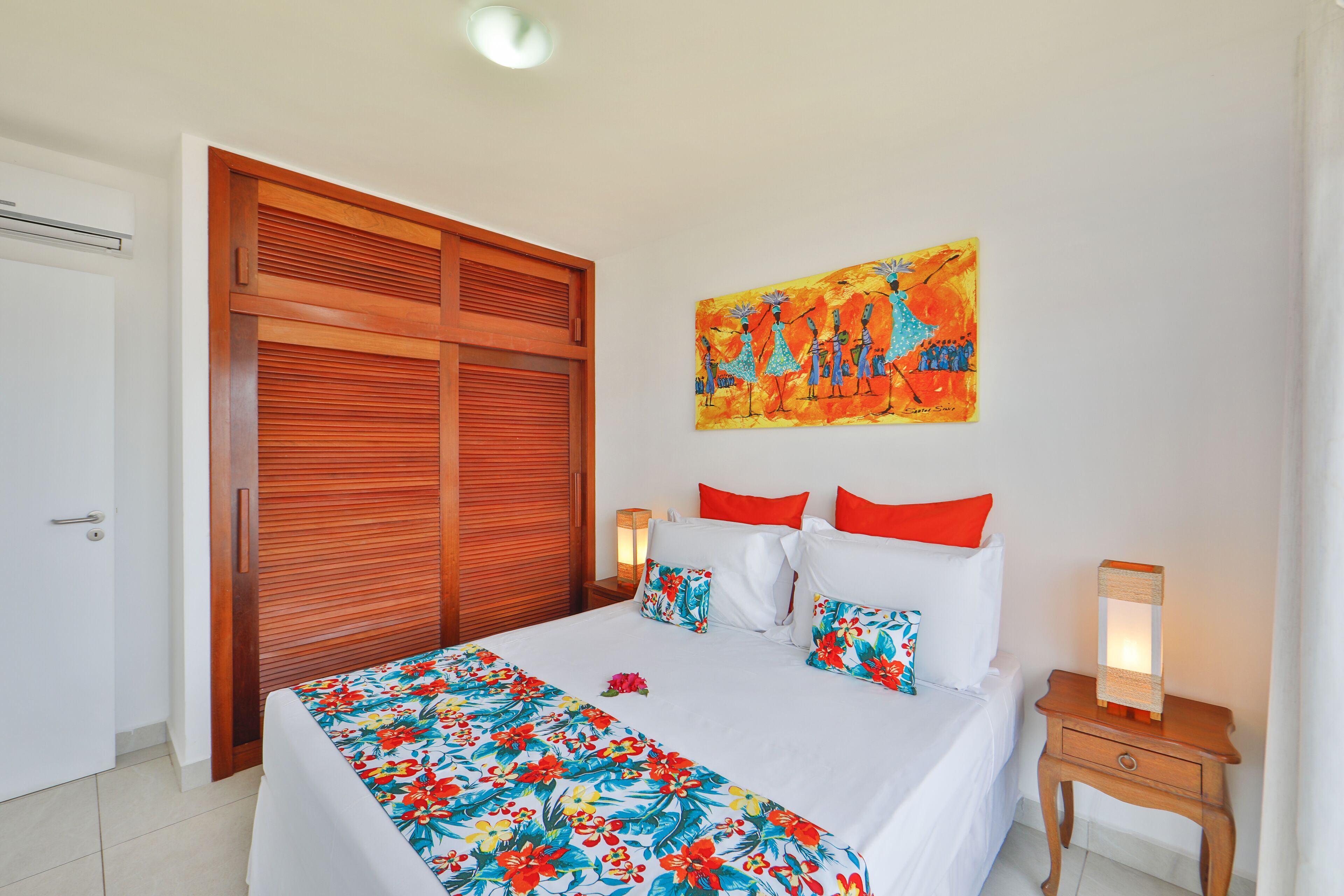 Camera da letto con un letto, armadio in legno, opere d'arte, cuscini, lampade sui comodini e una coperta con motivi floreali.