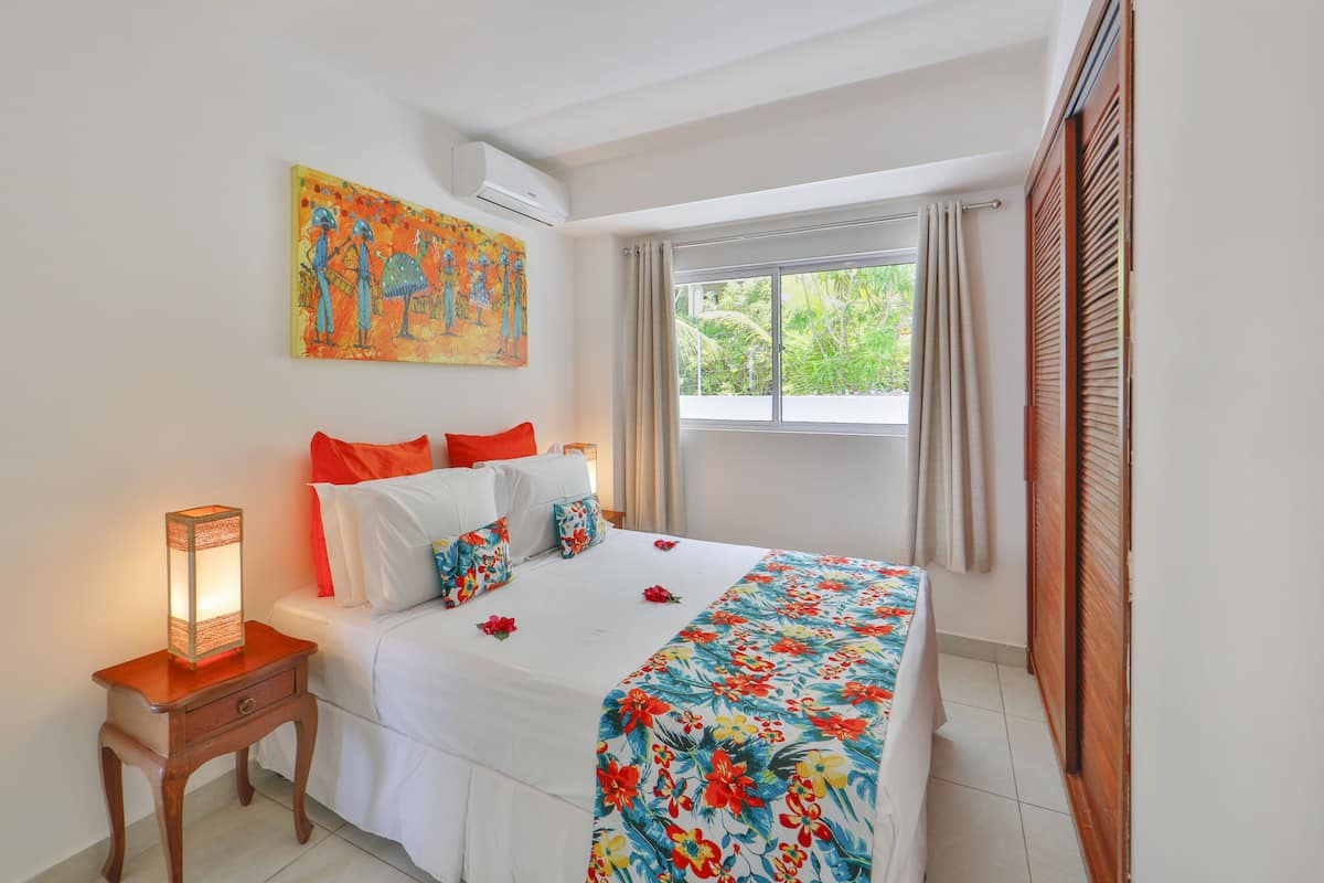 A bedroom with a bed, a nightstand, a window with curtains, and a painting on the wall.