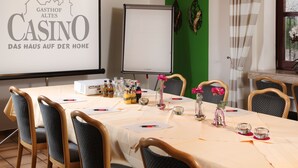 Een vergaderruimte met een projectiescherm waarop een logo staat, een whiteboard, en een tafel gedekt voor een vergadering met stoelen, documenten en decoratieve elementen.