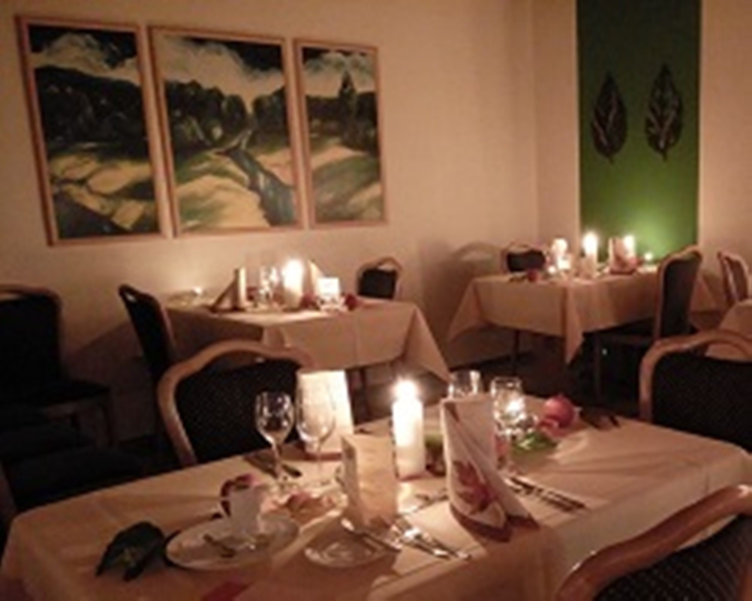 A dining area with tables set for two, candles, and framed artwork on the wall.