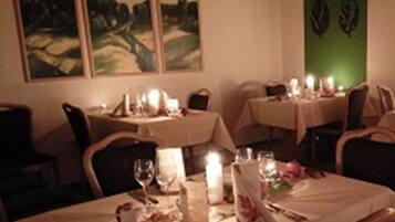 A dining area with tables set for two, candles, and framed artwork on the wall.