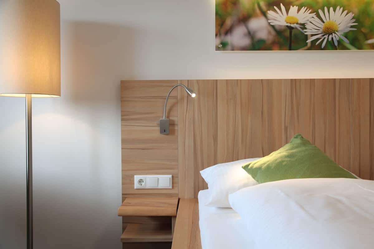 A neatly arranged hotel room with a bed, a nightstand, a lamp, and a wall-mounted light fixture.