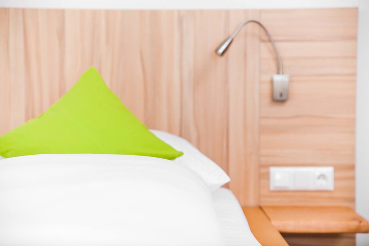 A bed with white and green pillows, a wooden headboard, and a nightstand with a lamp.