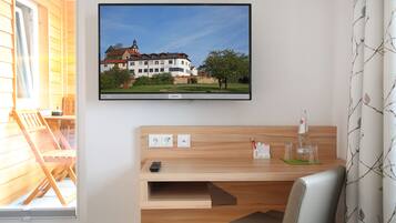Ein Hotelzimmer mit Holztisch, Wandfernseher und einem Fenster mit Jalousien.