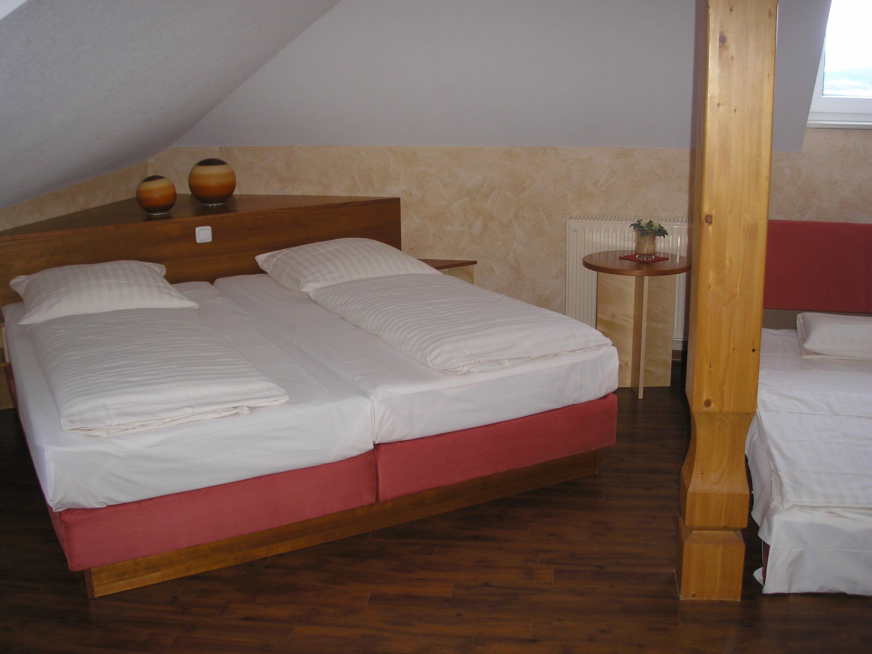 A double bed with a wooden headboard, a small bedside table with a vase, and a radiator in the background.