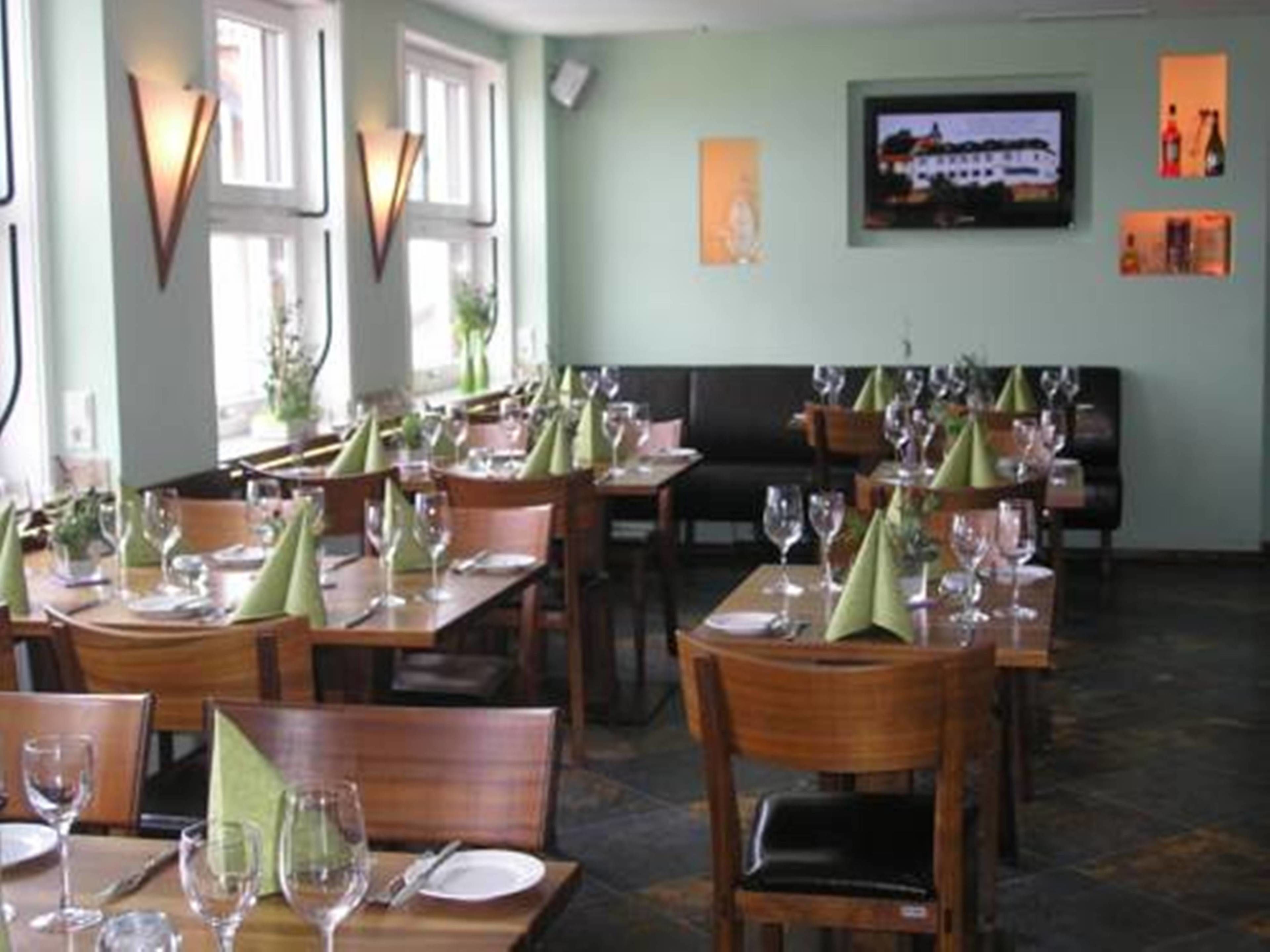 Ein Restaurant mit mehreren Essplätzen, jeweils mit grünen Servietten und Weingläsern.