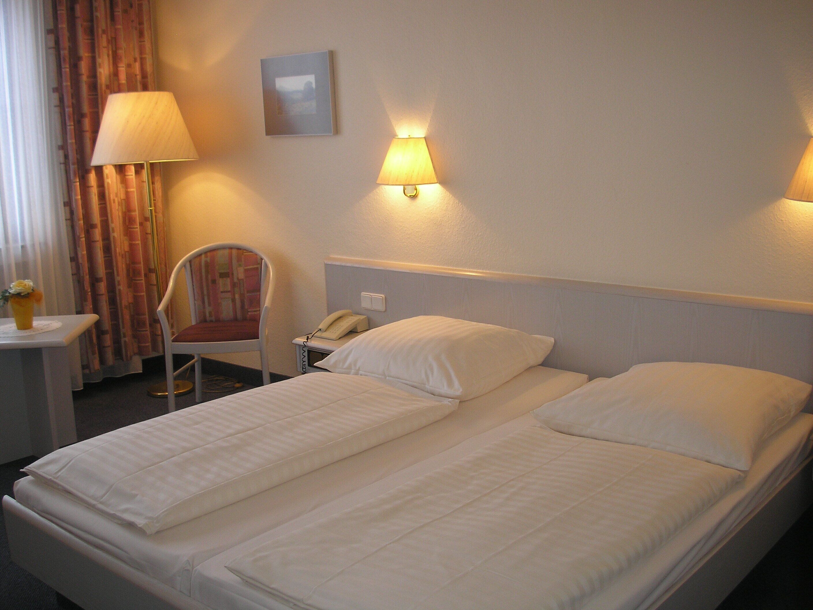 A hotel room with two beds, a chair, a desk with a lamp, and a telephone.