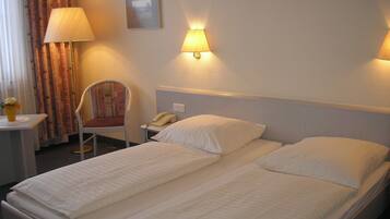 A hotel room with two beds, a chair, a desk with a lamp, and a telephone.