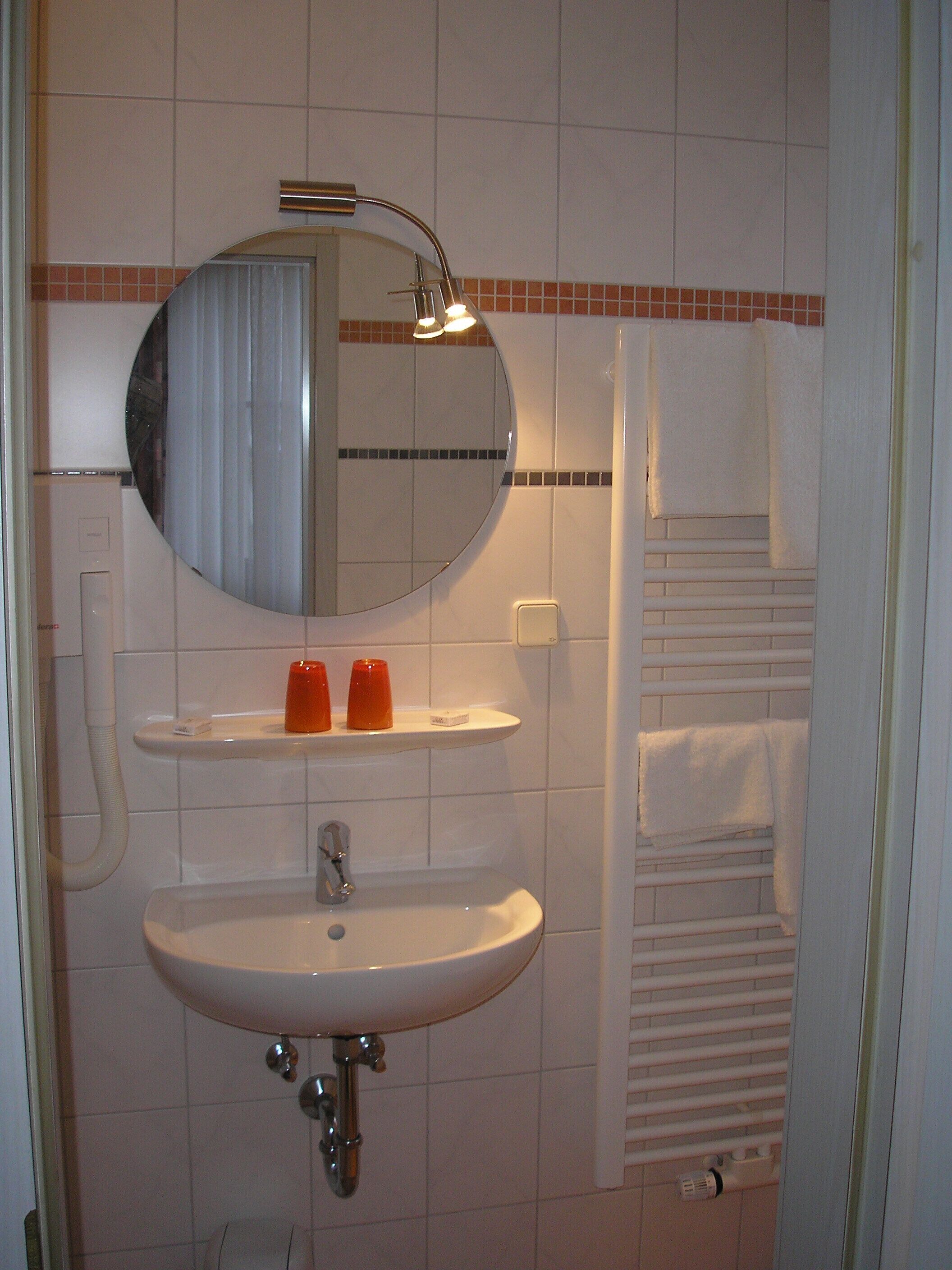 Ein Badezimmer mit einem weißen Waschbecken, einem runden Spiegel und einem Handtuchhalter.