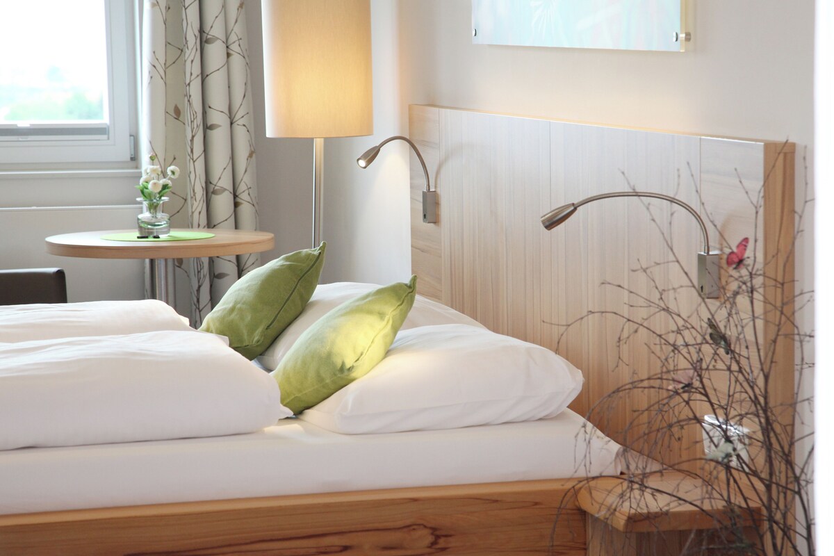 Une chambre d’hôtel avec un lit en bois, une petite table ronde ornée d’un vase de fleurs et une lampe.