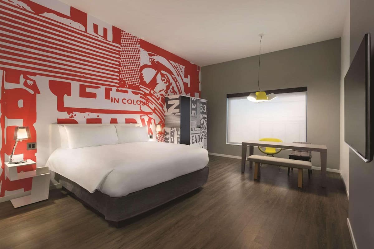 A modern hotel room with a large bed, a desk, and a wall mural.