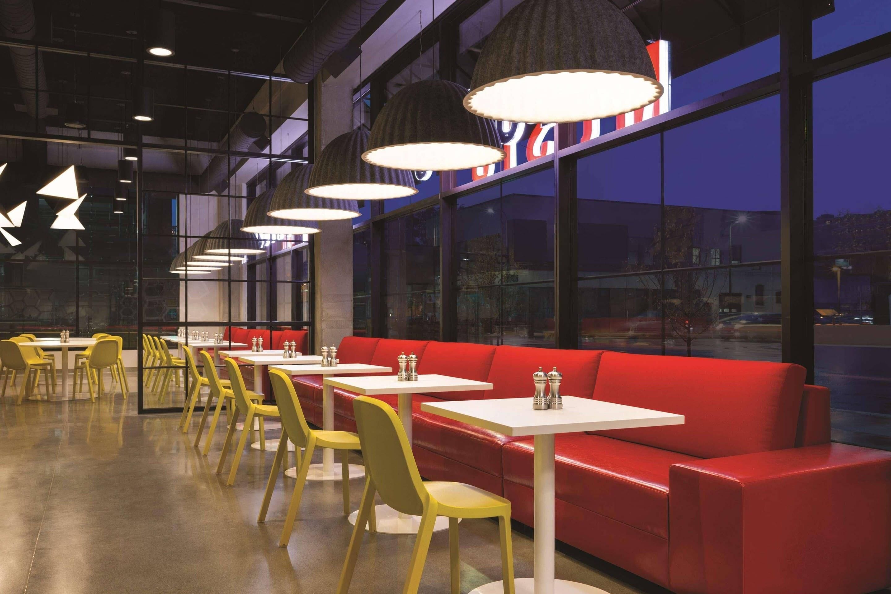 Interior de restaurante con sillas amarillas, asientos rojos e iluminación colgante.