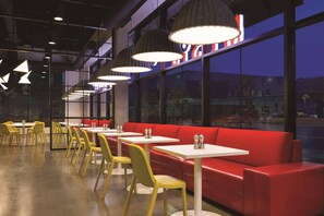 Interior de restaurante con sillas amarillas, asientos rojos e iluminación colgante.