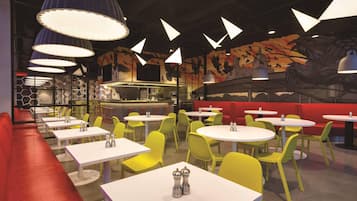 A restaurant interior with round tables, yellow chairs, red seating, and a mural with birds.