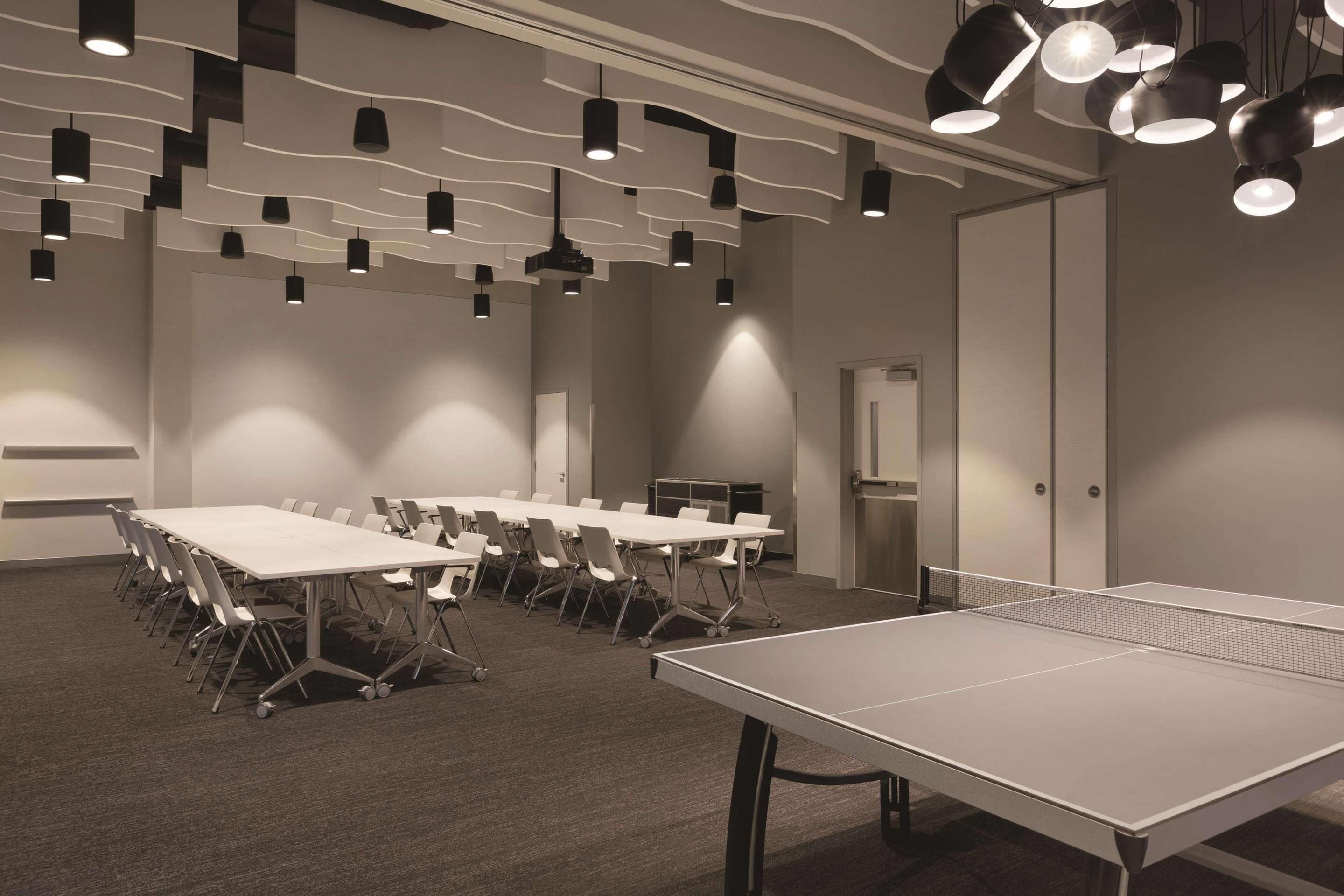 Un salón de conferencias con mesas y sillas, una mesa de ping-pong e iluminación colgante moderna.