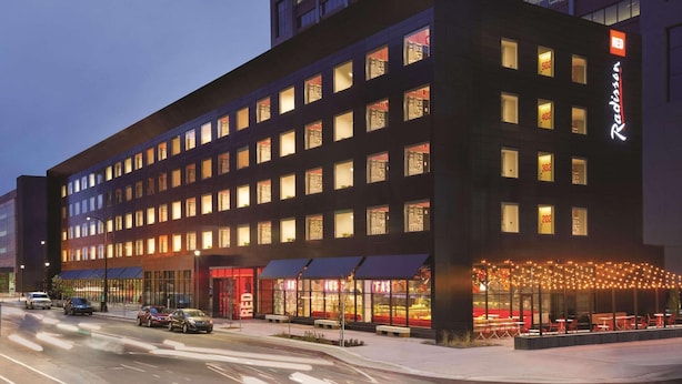 A modern hotel with multiple floors, large windows, and a well-lit entrance area with outdoor seating. - Radisson RED Minneapolis Downtown (Minneapolis)