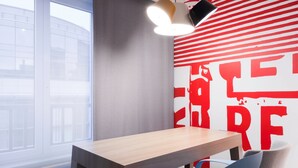 Un espacio de oficina moderno con una mesa de madera y dos sillas, un ventanal grande y una pared con arte abstracto rojo.