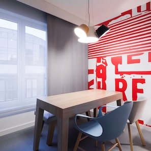 Un espacio de oficina moderno con una mesa de madera y dos sillas, un ventanal grande y una pared con arte abstracto rojo.