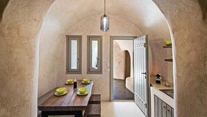 Un pasillo estrecho con una mesa de madera y cuencos verdes, que conduce a una cocina con armarios y una lámpara colgante.