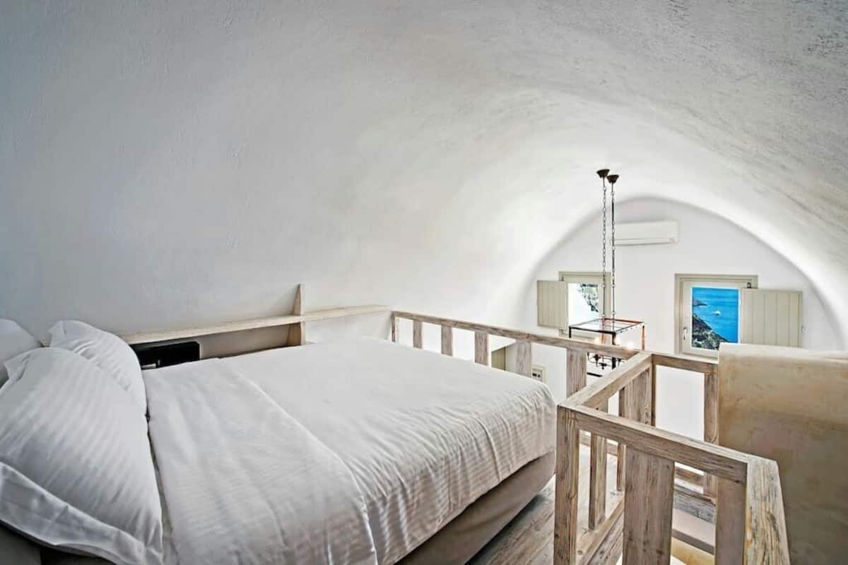 A bedroom with a wooden bed frame, white bedding, and a view of the sea through a window.