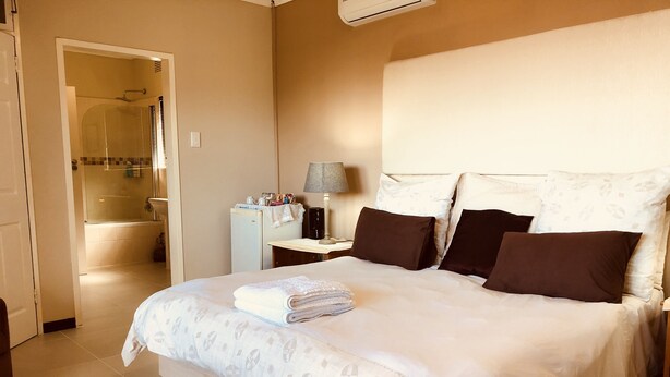 A neatly made bed with a patterned duvet, a bedside lamp, and a nightstand with toiletries. - Eden Rose Manor (La Mercy)