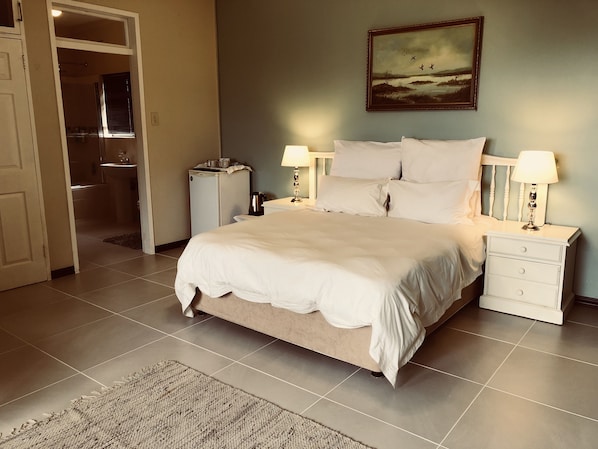 Un dormitorio con una cama, dos mesitas de noche con lámparas, un cuadro en la pared y una puerta que da al baño.