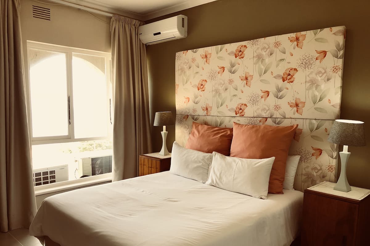 A hotel room with a large bed, floral wallpaper, two bedside tables with lamps, and a window with curtains.